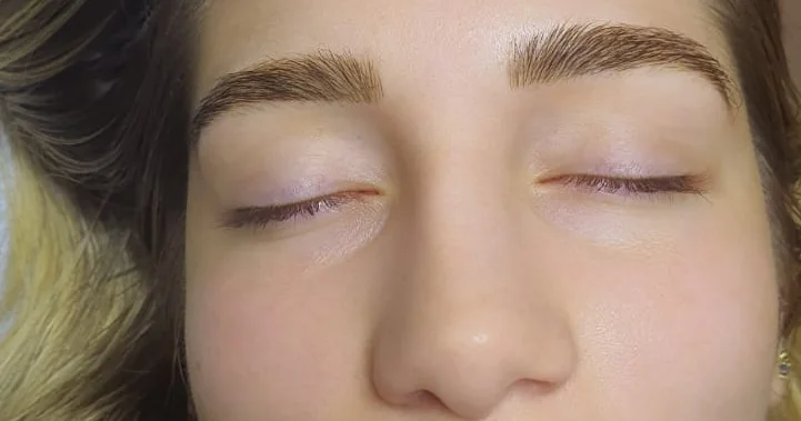 Mulher fazendo cuidados pós-micropigmentação nas sobrancelhas com cotonete e pomada cicatrizante.